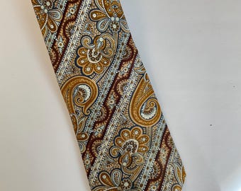 May include: A brown, blue, and white paisley patterned tie. The tie has a pointed tip and a diagonal stripe pattern.