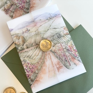 May include: A white invitation card with a watercolor illustration of a vineyard landscape. The card is sealed with a gold wax seal with a floral design. The card is on top of a green envelope.