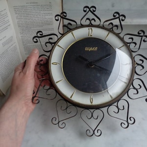 May include: A vintage black and white clock with a gold trim and black hands. The clock is surrounded by a decorative metal frame with a heart design.