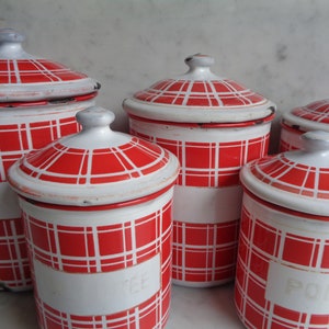 Peut inclure: Ensemble de cinq boîtes en émail rouge et blanc avec couvercles. Les boîtes ont un motif à carreaux et sont étiquetées avec les mots "Sucre", "The", "Farine" et "Poivre".