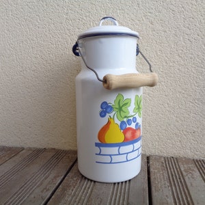 Puede incluir: Bote de leche de esmalte blanco con borde azul y asa de madera. El bote tiene un diseño de frutas con una pera, uvas y hojas.