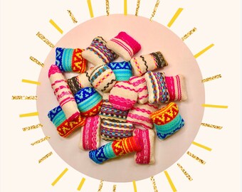 May include: A cluster of small, rectangular woven cushions in diverse colours, such as pink, blue, and orange. The cushions feature striped and patterned designs. The arrangement is on a light pink circle with a gold sunburst design.