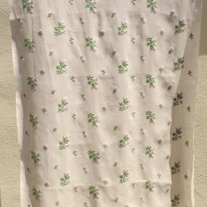 May include: A white fabric with a repeating pattern of small pink and green flowers. The fabric is hanging on a clothesline.
