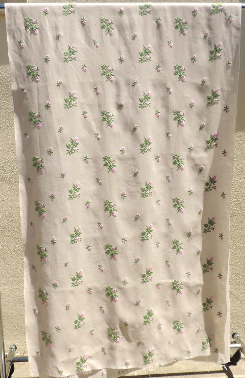 May include: A white fabric with a repeating pattern of small pink and green flowers. The fabric is hanging on a clothesline.