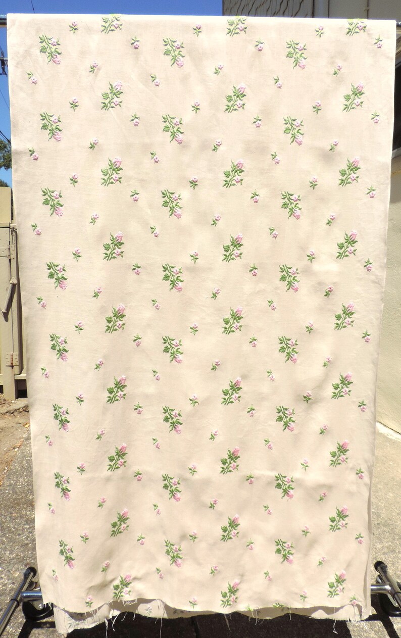 May include: A cream-colored fabric with a repeating pattern of pink and green embroidered flowers.