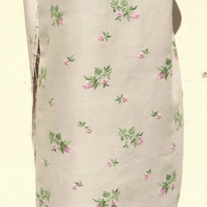 May include: A beige fabric with a delicate floral pattern. The fabric is embroidered with small pink roses and green leaves.