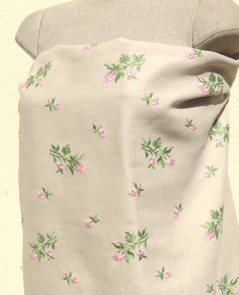 May include: Beige fabric with a delicate floral pattern featuring pink flowers and green leaves. The fabric is smooth and has a subtle sheen.