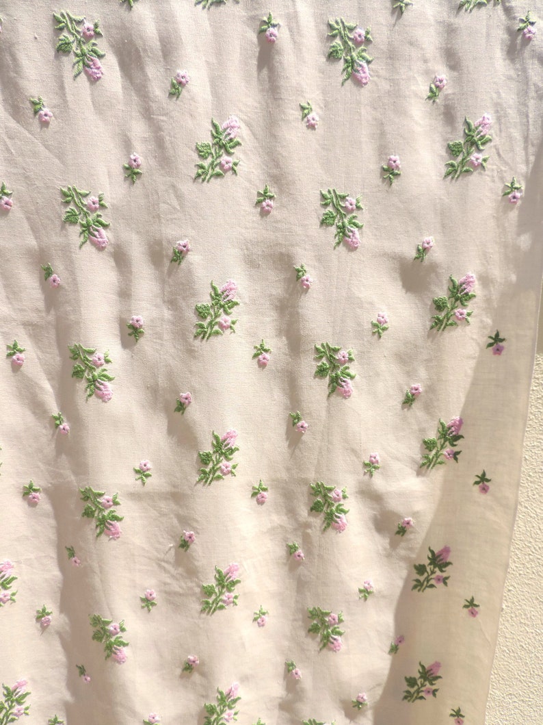 May include: White fabric with a delicate floral pattern embroidered in pink and green. The fabric has a subtle texture and a soft, light feel.
