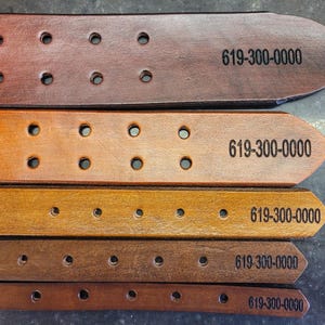 May include: Five leather belts in different shades of brown, each with a row of holes and the text "619-300-0000" printed on them.