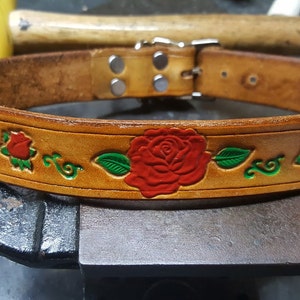 May include: A brown leather dog collar with a silver buckle and red roses with green leaves embossed on the surface.