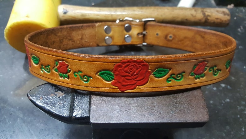 May include: A brown leather dog collar with a silver buckle and red roses with green leaves embossed on the surface.