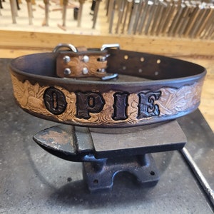May include: A brown leather dog collar with a tooled floral design and the name "OPIE" embossed in black lettering.
