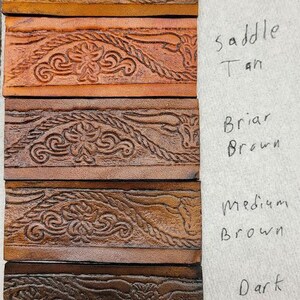May include: Leather swatches in various shades of brown, from mahogany to antique black, with a decorative embossed pattern of a bull's head and rope design. The swatches are labeled with their corresponding color names.