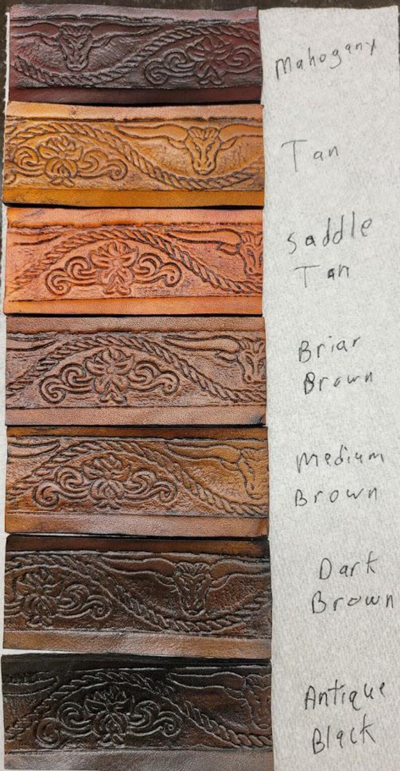 May include: Leather swatches in various shades of brown, from mahogany to antique black, with a decorative embossed pattern of a bull's head and rope design. The swatches are labeled with their corresponding color names.