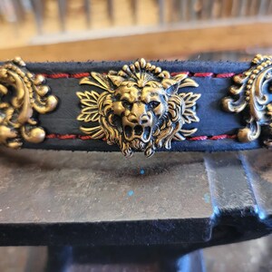 May include: A black leather collar with red stitching and gold metal lion head and floral design accents.