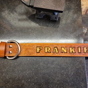 May include: A brown leather dog collar with silver hardware and the name "FRANKIE" embossed in gold lettering.