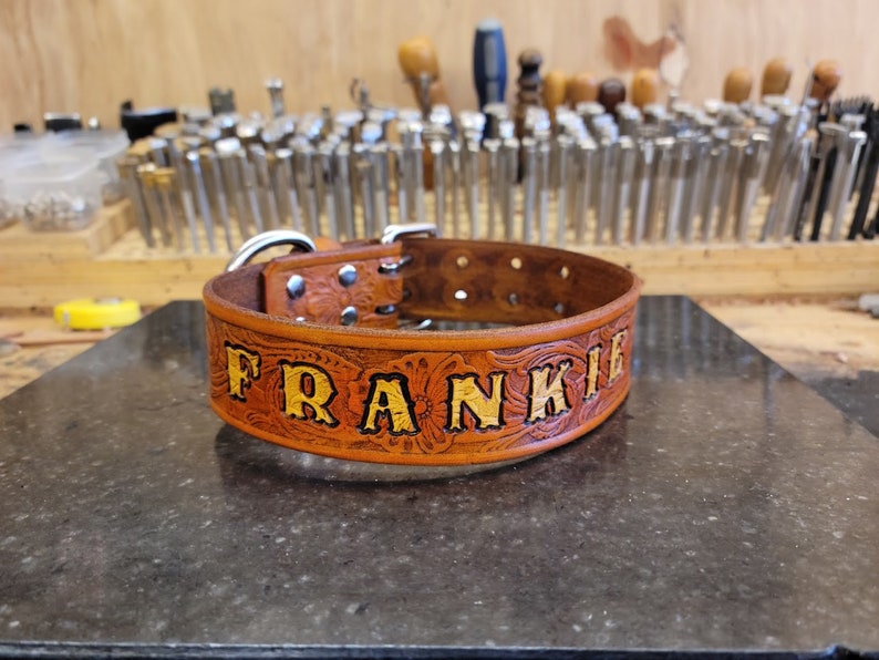 May include: A brown leather dog collar with silver hardware and the name "FRANKIE" embossed in gold lettering.
