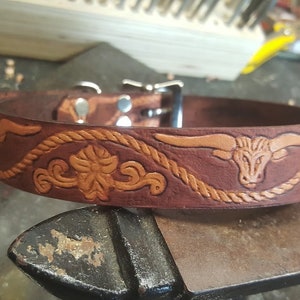 May include: A brown leather dog collar with a tooled design featuring a bull's head and a rope pattern.