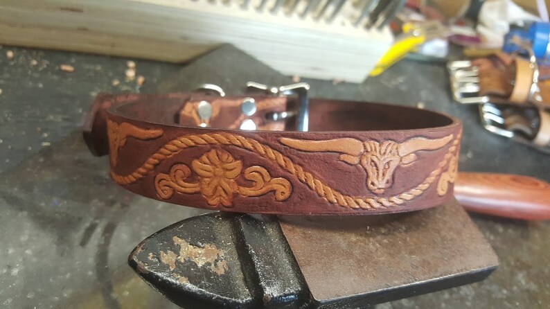 May include: A brown leather dog collar with a tooled design featuring a bull's head and a rope pattern.