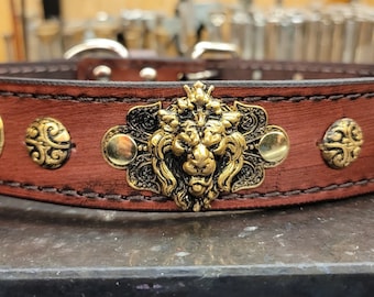 May include: A brown leather dog collar with gold-toned metal accents. The center accent features a lion's head design.