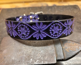 May include: A black leather dog collar with a purple floral design. The collar is embossed with a repeating pattern of flowers and circles.