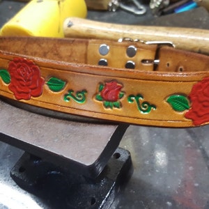 May include: A brown leather dog collar with a decorative design of red roses and green leaves.