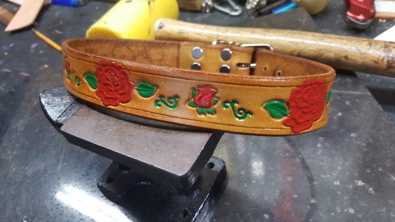 May include: A brown leather dog collar with a decorative design of red roses and green leaves.