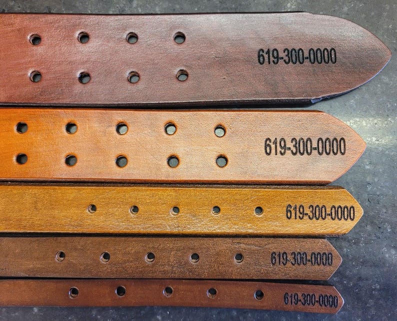 May include: Five leather belts in different shades of brown, each with a row of holes and the text "619-300-0000" printed on them.