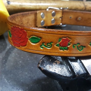 May include: A brown leather dog collar with a silver buckle and red roses with green leaves embossed on the surface.