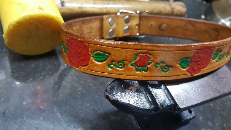 May include: A brown leather dog collar with a silver buckle and red roses with green leaves embossed on the surface.