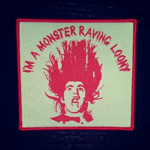 Puede incluir: Un parche bordado rojo y blanco con el texto "I'm a Monster Raving Loony" y una silueta de una persona con el pelo de punta.
