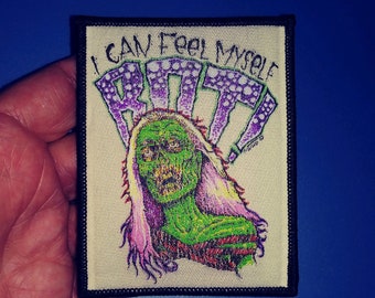 Puede incluir: Un parche bordado en blanco y negro con una figura verde de zombie con cabello morado. El texto "I can feel myself ROTTING" está por encima de la figura.