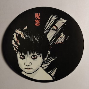 May include: Black and white illustration of a young person with black hair and a white face, with a long-haired figure with a white face behind them. The figure behind them has a long, dark, flowing hair and a white face. The text "呪怨" is in red on the black background.
