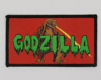 May include: A red, black, and green embroidered patch with the word "GODZILLA" in green dripping letters and a green and brown Godzilla monster with a yellow beam shooting from its mouth.