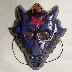 May include: A dark blue wolf mask with a red pentagram on the forehead and red accents around the eye holes. The mask has a black string for wearing and a crown design at the top.