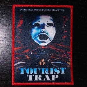 May include: Red, white, and blue embroidered patch with the text "Tourist Trap" and the phrase "Every year young people disappear."  A creepy, masked face is in the background.