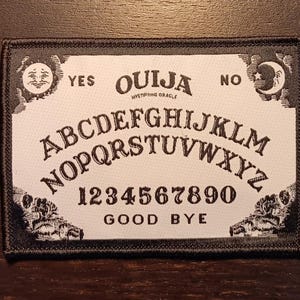 May include: Black and white ouija board patch with the letters A-Z, numbers 1-9, and the words "YES", "NO", "OUIJA", "GOOD BYE", and "MYSTIFYING ORACLE".