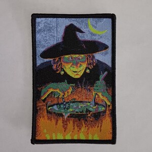 Puede incluir: Una bruja con la cara verde y un sombrero negro remueve una caldera con una cuchara de madera. La caldera está sobre un fuego y hay una luna creciente en el fondo.
