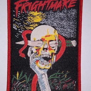Peut inclure: Patch brodé noir et rouge avec le texte "FRIGHTMARE" en blanc. Le patch représente un crâne blanc avec un effet de goutte rouge et jaune, une main rouge et jaune tenant le crâne et de l'herbe verte.