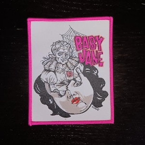 Peut inclure: Un écusson thermocollant blanc avec une bordure rose. L'écusson représente une illustration en noir et blanc d'une femme avec une tête de femme à l'intérieur de sa tête. Le texte "BABY JANE" est écrit en lettres roses.