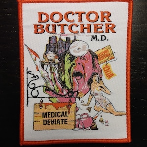 May include: A white embroidered patch with an orange border. The patch features a graphic of a doctor with a bloody knife and a sign that reads "Medical Deviate". The text "Doctor Butcher M.D." is at the top of the patch.