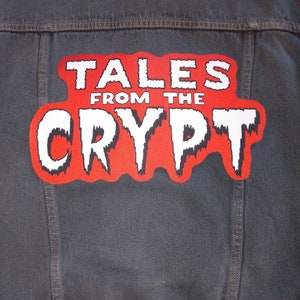 May include: A red and white patch sewn onto a denim jacket with the text "Tales from the Crypt" in a dripping font.