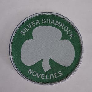 May include: A green and white embroidered patch with the text "Silver Shamrock Novelties" and a white shamrock design.