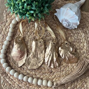 May include: Four gold oyster shell ornaments with a gold tassel and a wooden bead garland. The ornaments are hanging from gold ribbon.