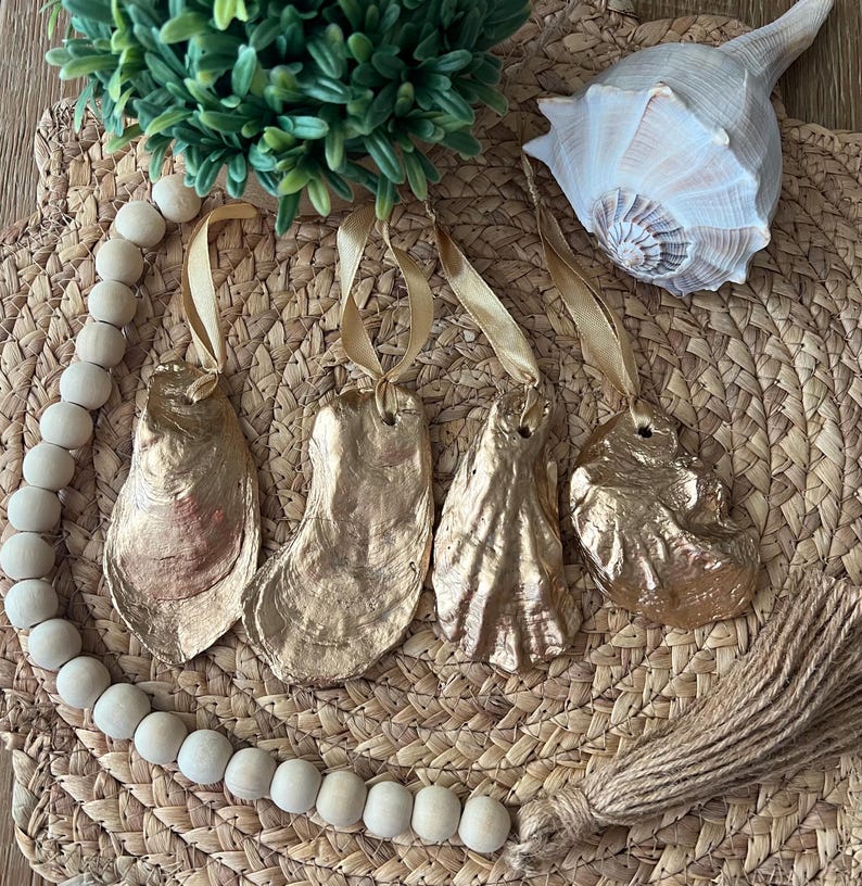 May include: Four gold oyster shell ornaments with a gold tassel and a wooden bead garland. The ornaments are hanging from gold ribbon.