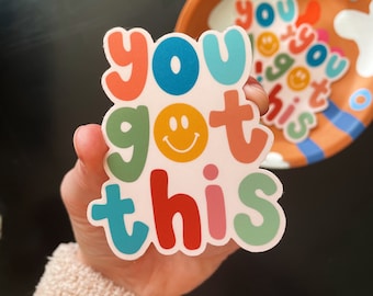 May include: A colorful sticker with the phrase "you got this" in various colors, including red, blue, green, and orange. A smiling face replaces the letter "o" in "got". A matching plate with the same phrase is in the background.