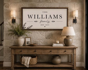 Peut inclure: Une enseigne murale rectangulaire avec un cadre en bois foncé et un fond blanc, présentant le texte noir THE WILLIAMS family EST. 2023, orné de petites illustrations de feuilles et d'un symbole de cœur centré sous la date établie.