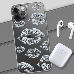 May include: A clear phone case with a pattern of silver lips. The case is designed for an iPhone with a triple lens camera. The case is shown on a gray surface with a pair of white wireless earbuds and a white charging case.