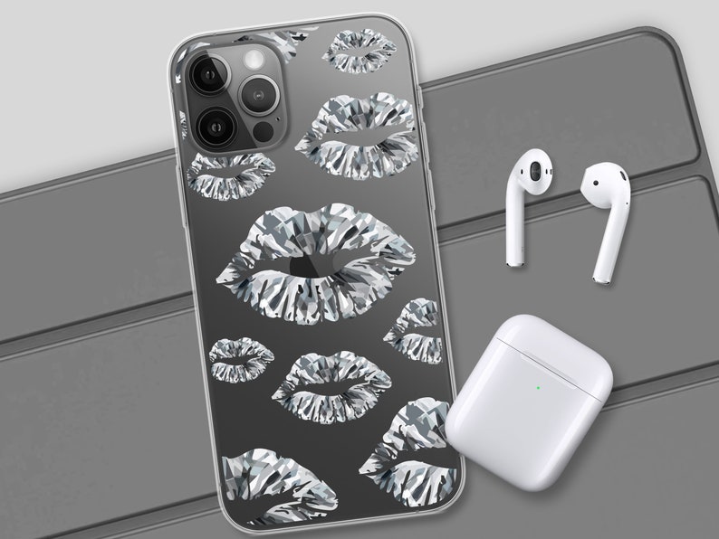 May include: A clear phone case with a pattern of silver lips. The case is designed for an iPhone with a triple lens camera. The case is shown on a grey surface with a pair of white wireless earbuds and a white charging case.