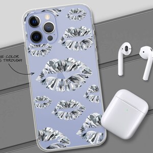 May include: A clear phone case featuring a design of silver glitter lips on a light purple background. The case is displayed on a grey surface with a pair of white wireless earbuds and a white charging case.